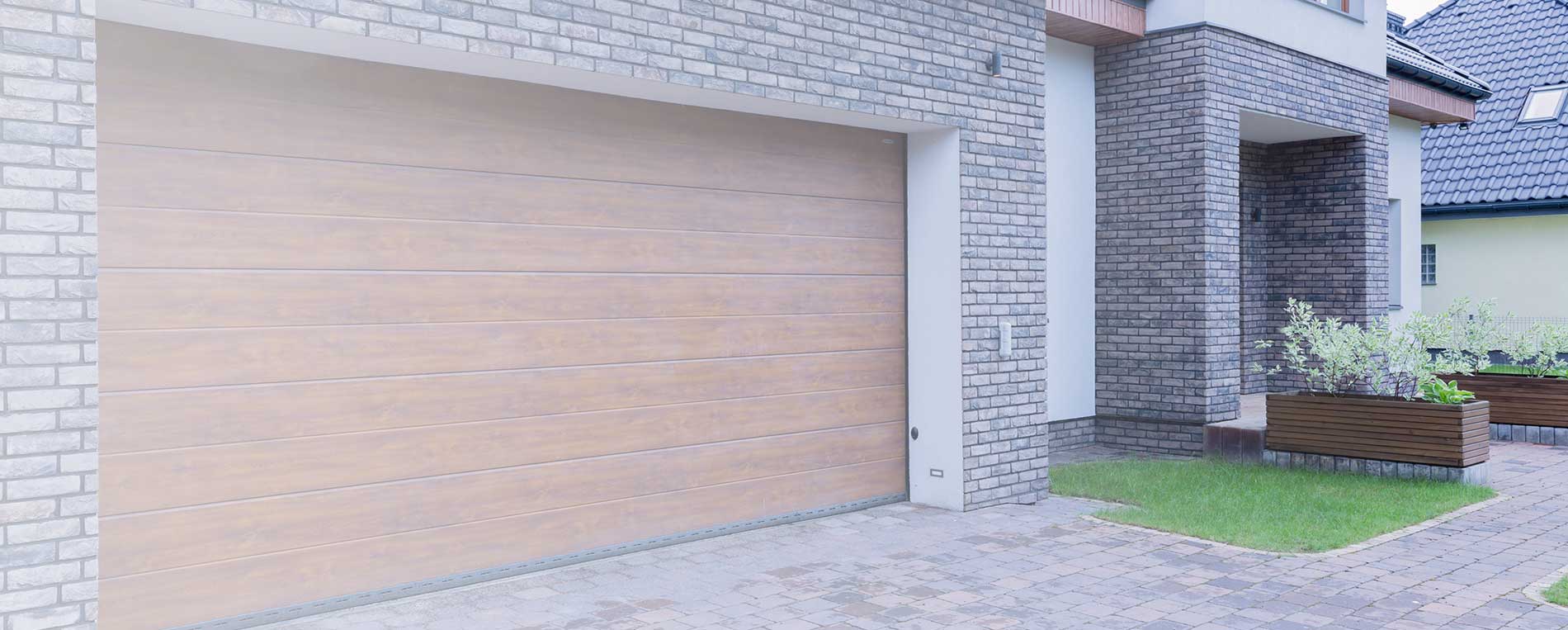 Contemporary residential garage door with sleek wooden finish, installed on a modern brick house.