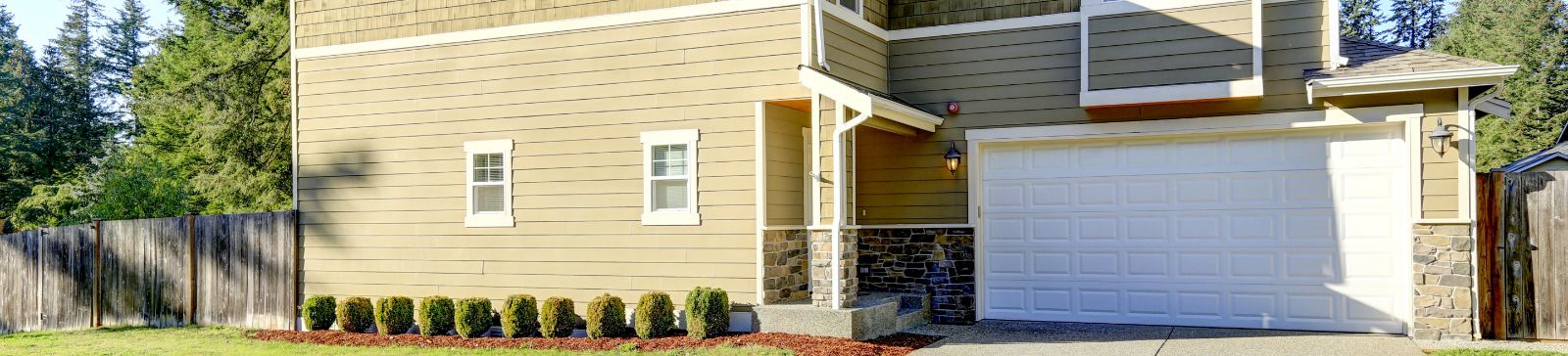 Tan house with a clean, white overhead garage door and neat landscaping in Lakeside.